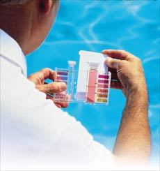 A man by a swimming pool checking pool water quality.