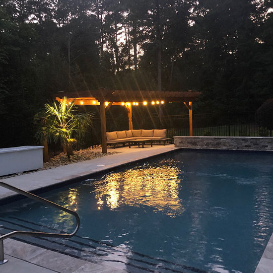 an outdoor living space with cozy sitting places and lights placed by a backyard swimming pool