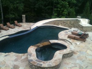 A residential outdoor swimming pool and hot tub with a flagstone deck designed and installed by Premier Pool Inc.