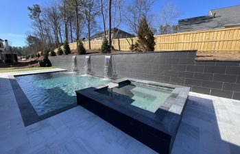 Backyard swimming pool with a hardscaped hot tub and waterfalls installed by Premier Pool Enterprises