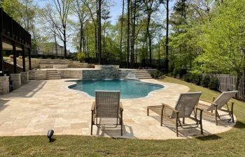 Pool chairs on a deck of a modern backyard pool with water features